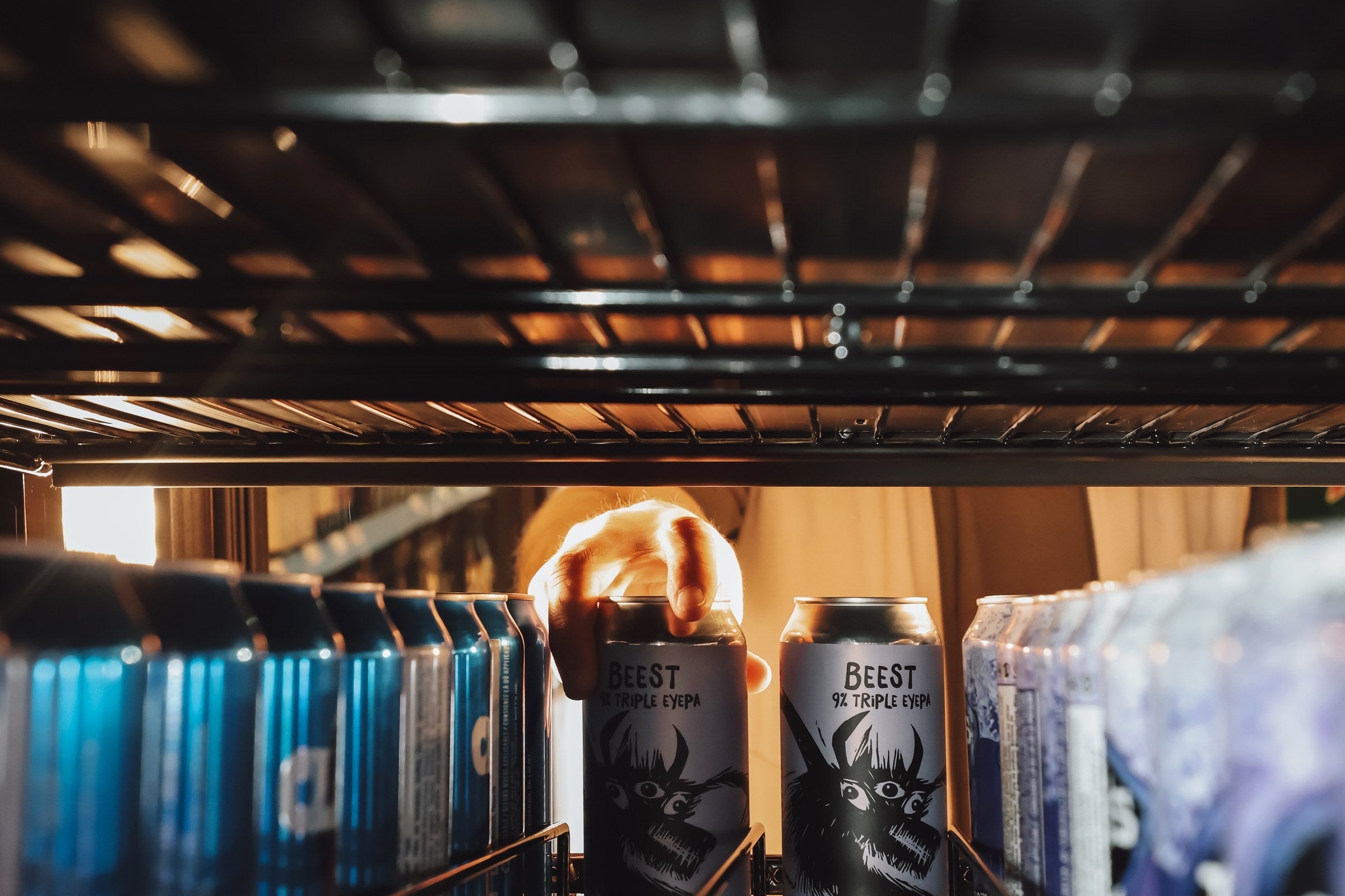Hand grabbing a craft beer from the fridge at 1933 Liquor Co